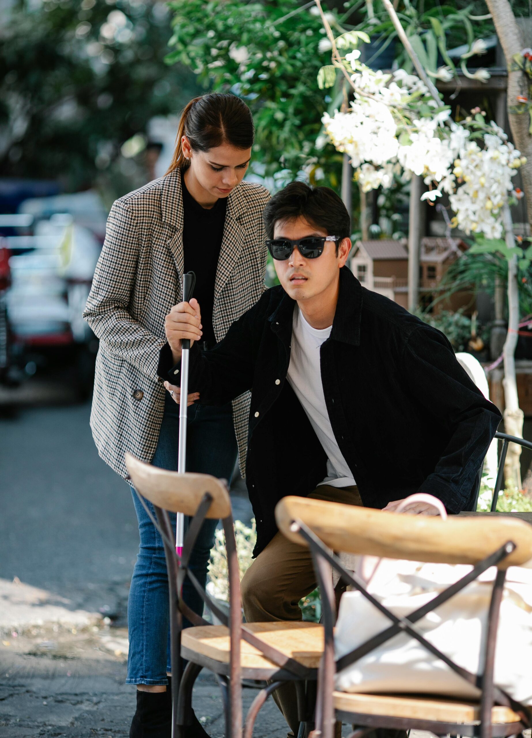 A caregiver assists a blind man using a walking stick outdoors, symbolizing care and support.