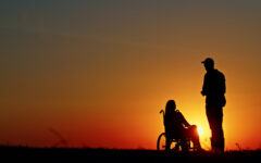 Silhouette of a person standing beside a woman in a wheelchair during a beautiful sunset. A scene symbolizing support, companionship, and hope under the golden glow of dusk.
