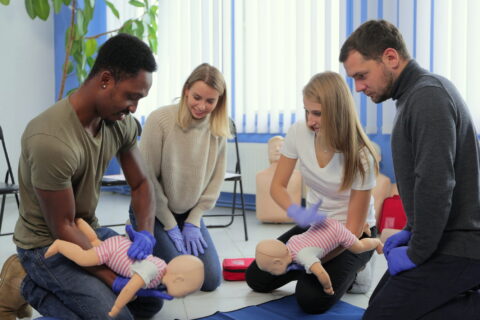 Group of multiethnic people during the first aid training with instructor showing on manikin how to do artificial respiration for the baby.