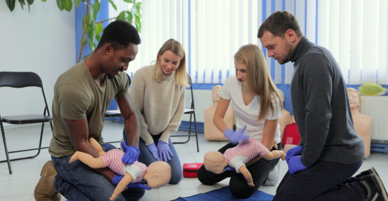 Group of multiethnic people during the first aid training with instructor showing on manikin how to do artificial respiration for the baby.