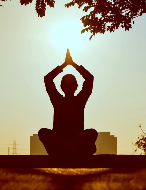 Silhouette of a person practicing yoga outdoors during sunrise, creating a calming atmosphere.